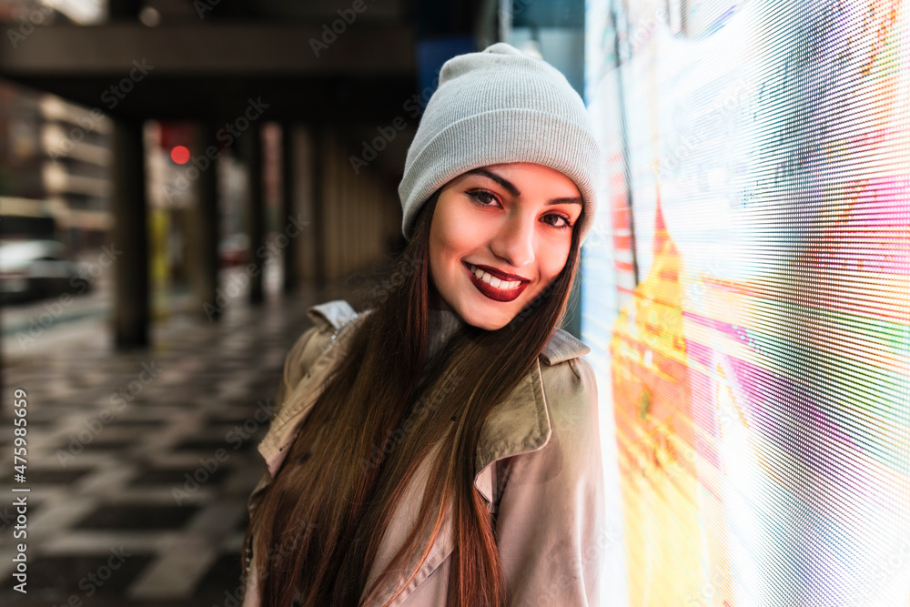 Smiling young woman leaning on illuminated glass wall Smiling young woman leaning on illuminated glass wall