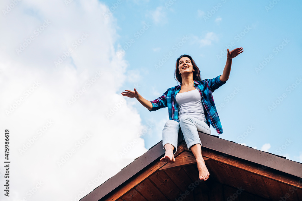 Woman with arms outstretched sitting on top of house roof Woman with arms outstretched sitting on top of house roof