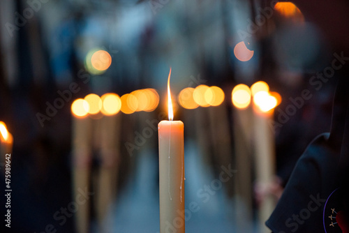 selective focus detail of a lighted candle carried by a penitent, during a Holy Week procession in Spain, with out-of-focus lights of those next in line