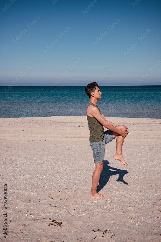 Young man practices yoga on the beach near the blue ocean. Meditation and exercise of an athletic guy.