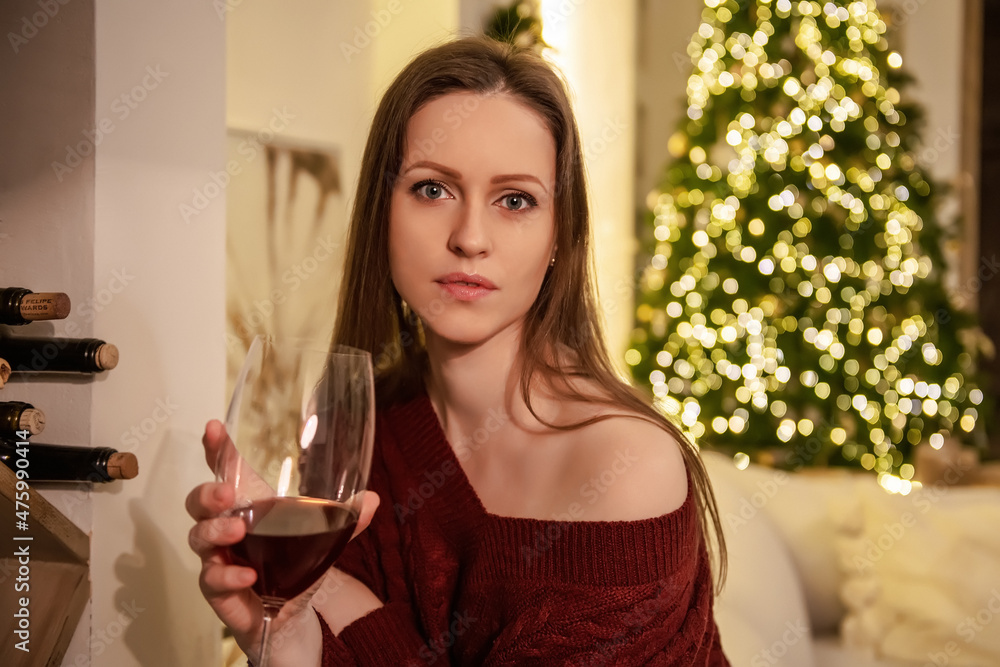A beautiful young woman on a couch with a glass of wine against the background of a New Year tree and Christmas decorations, waiting for the holiday. A beautiful young woman on a couch with a glass of wine against the background of a New Year tree and Christmas decorations, waiting for the holiday.
