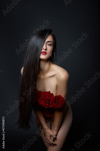 Beautiful brunette woman with a bouquet of red rose flowers in red corset. Long hair, nude slim body art portrait