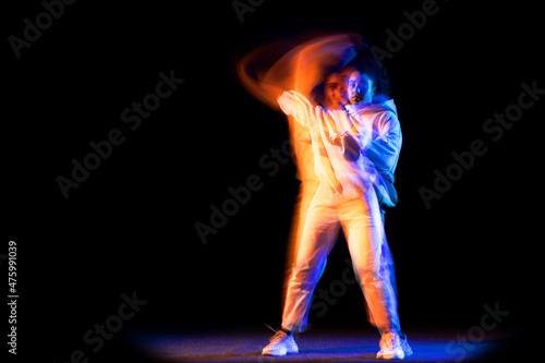 Emotinal young girl in white hoodie dancing hip-hop dance isolated on dark background in purple neon mixed light.
