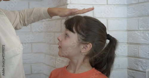 Child being measured. A view of smiling happy little girl being measured by the white wall in the room. photo