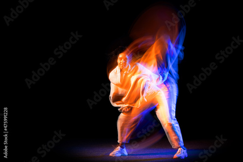 Sportive young girl in white costume dancing hip-hop dance isolated on dark background at dance hall in neon mixed light.