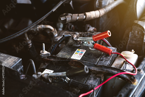 Charging old car battery by using electricity trough red and black jumper cables. Car maintenance concept.