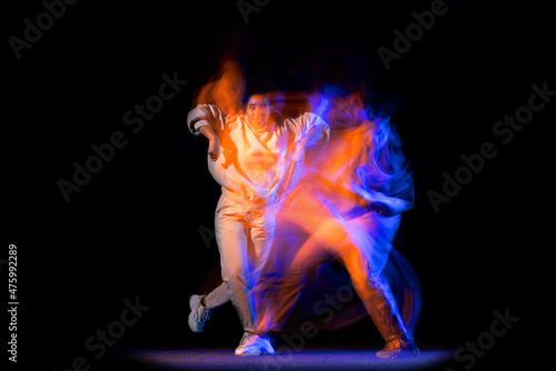 Portrait of young dark skinned flexible girl in white hoodie dancing hip-hop isolated on dark background in purple neon mixed light. © master1305
