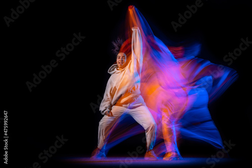 One sportive girl, hip-hop dancer practicing alone at stage on dark background in purple neon mixed light.