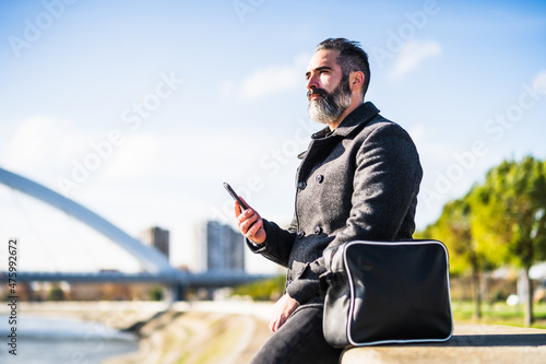 Businessman is sitting outdoor in the city and using smartphone.