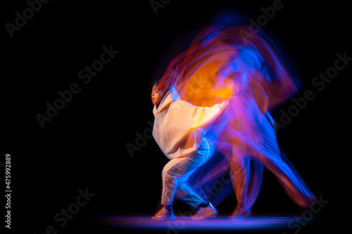 One sportive girl, hip-hop dancer practicing alone at stage on dark background in purple neon mixed light.