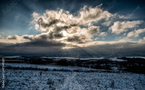 Winter snowy country and sunrays through clouds on sky