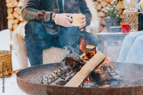 couple of young woman and man having fun, tenderness during teatime near fire in courtyard of suburban house in winter, concept of Christmas and New Year vacation on farm, family love and support