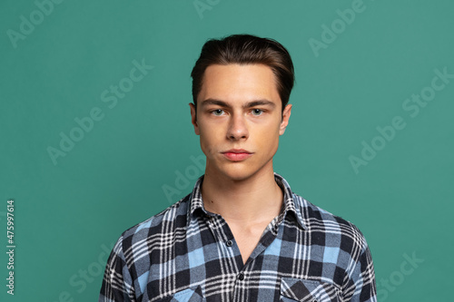 Close-up young handsome calm man, student wearing warm plaid shirt isolated on green studio background.