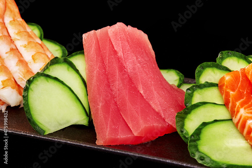 Closeup of raw tuna sashimi on platter with salmon, shrimp and cucumber