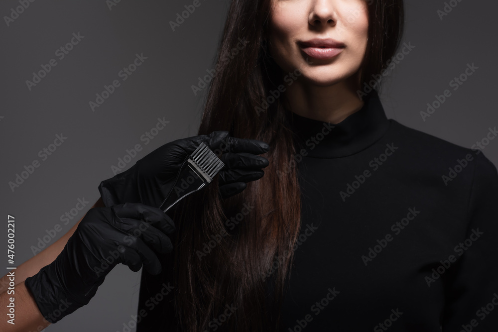 cropped view of hairstylist holding brush near woman with brown hair isolated on dark grey cropped view of hairstylist holding brush near woman with brown hair isolated on dark grey