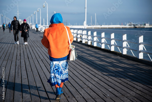 Starsza pani ubrana kolorowo spacerująca po molo.