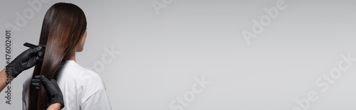 Foto colorist in latex gloves holding comb near long hair of client isolated on grey,