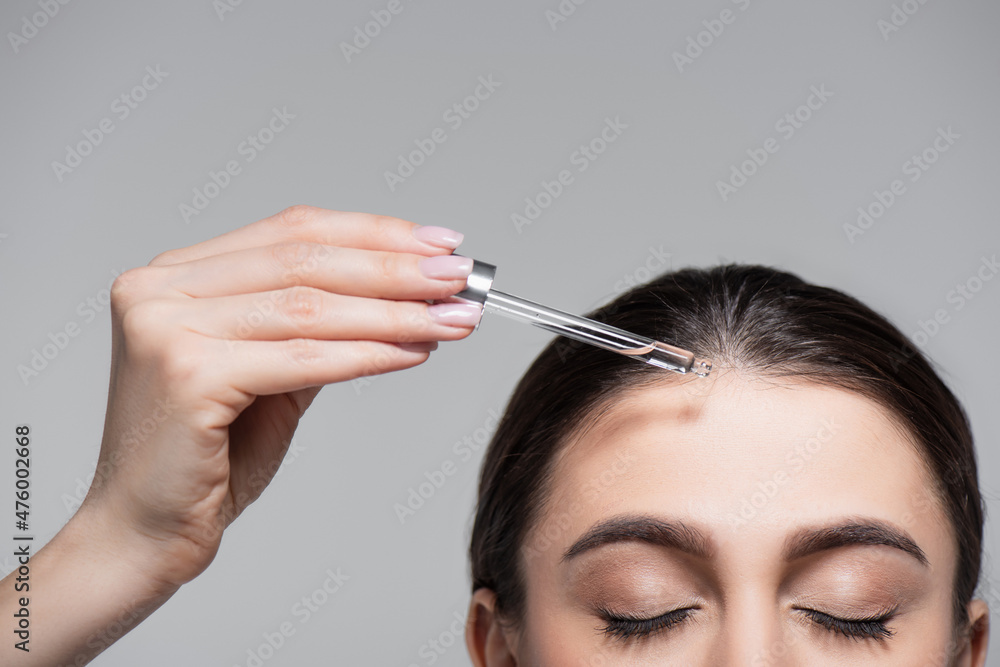 Fototapeta premium cropped view of young woman holding pipette with oil near shiny hair isolated on grey