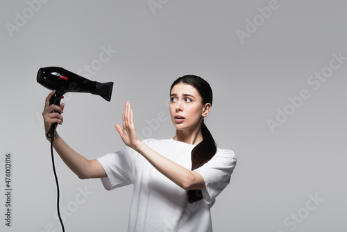 careful woman in white t-shirt holding hair dryer isolated on grey