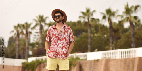 Canvas Print Tourist man on the beach standing outdoors against resort with palm trees in the background during summer holidays