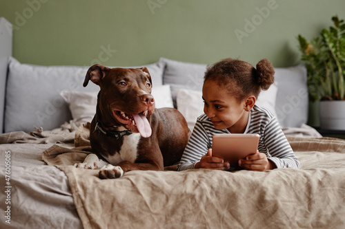 Fotografija Front view portrait of cute African-American girl lying on bed with big pet dog
