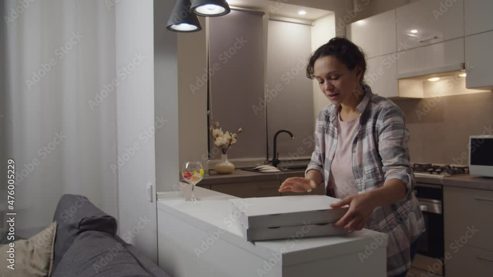 Attractive adult woman in casual clothing putting pizza boxes on kitchen counter at domestic room, opening carton, smelling pizza, smiling charmingly in anticipation of eating food at home Attractive adult woman in casual clothing putting pizza boxes on kitchen counter at domestic room, opening carton, smelling pizza, smiling charmingly in anticipation of eating food at home