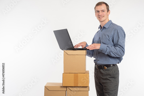 Small business. Delivery of goods. A young entrepreneur with a laptop and parcels. A businessman takes orders in an online store. E-business concept. Light background.