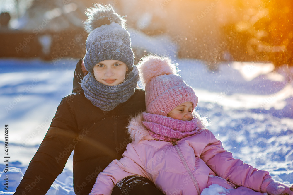 Two cute girls, the youngest and the oldest, are sitting in a winter park and playing with snow. Family values. Winter fun Two cute girls, the youngest and the oldest, are sitting in a winter park and playing with snow. Family values. Winter fun
