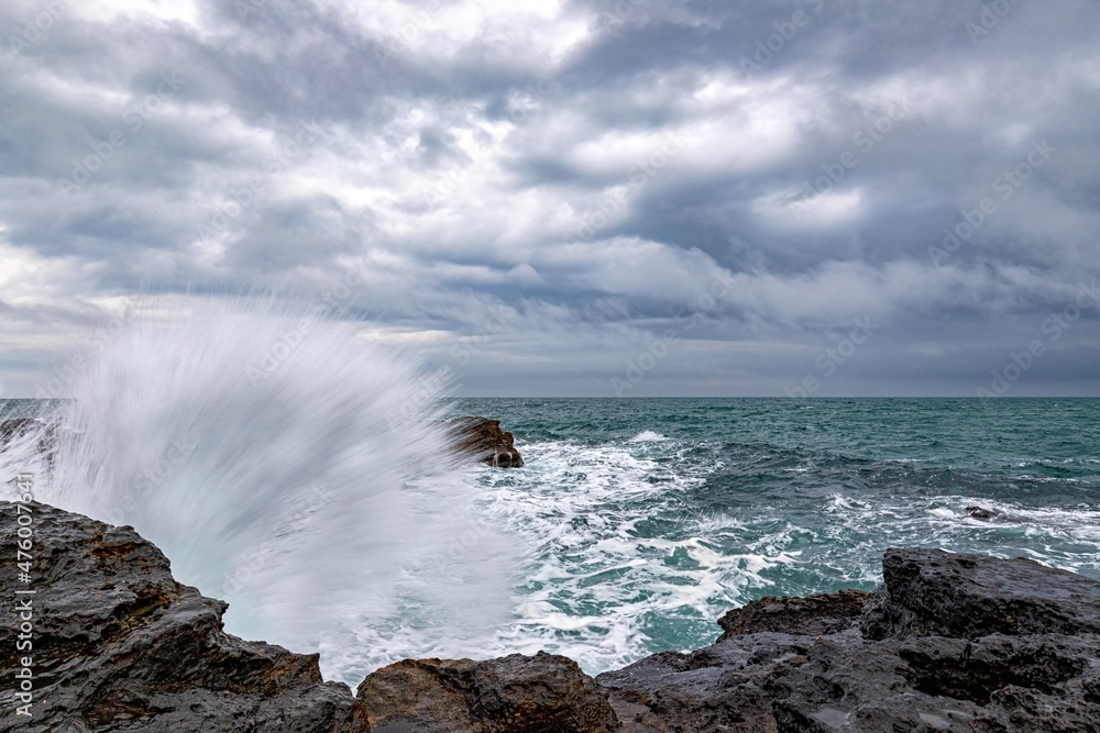 Stunning wave splash at rocky shore and scenic clouds