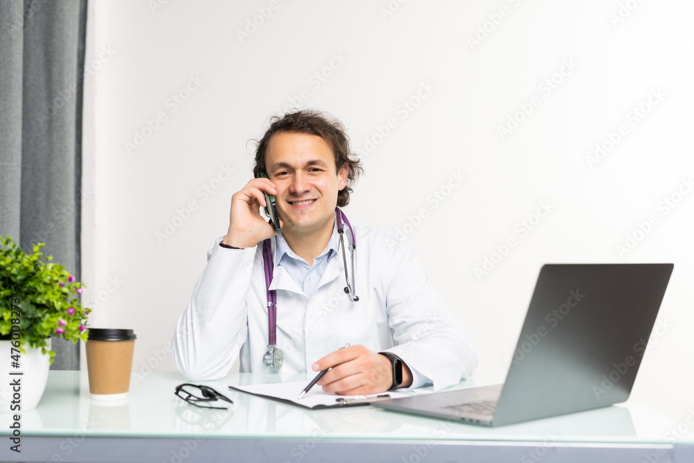 Happy doctor talking on phone with his patients and writing notes, working at his office Happy doctor talking on phone with his patients and writing notes, working at his office