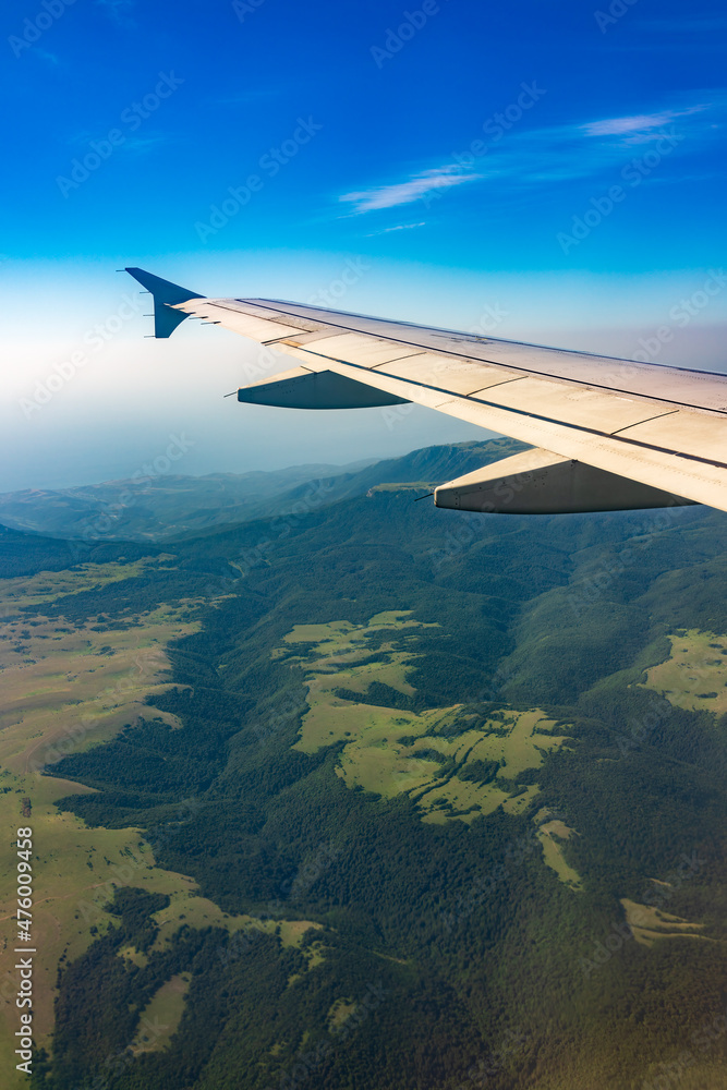 View of airplane wing, blue skies and green land during landing. Airplane window view. View of airplane wing, blue skies and green land during landing. Airplane window view.
