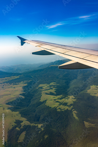 View of airplane wing, blue skies and green land during landing. Airplane window view.