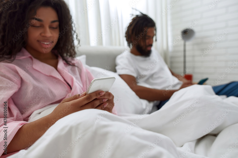 Young black couple watching on smartphones in bed