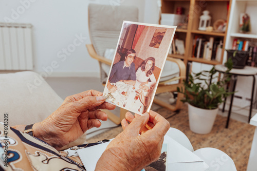Portrait of elderly woman hands looking at old picture of her dead husband made many years ago. Grandmother remembering memories of family members with nostalgia and melancholy at home.