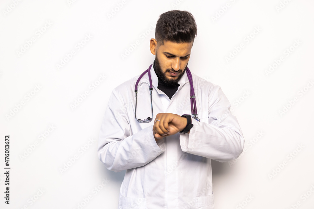 Indian doctor pointing at watch with serious expression as wasted time concept on white studio background Indian doctor pointing at watch with serious expression as wasted time concept on white studio background