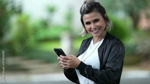 Happy Woman using smartphone device outside turning head to camera smiling
