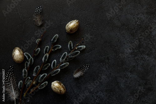 Happy Easter concept. Preparation for holiday. Golden decorated easter eggs willow feather on trendy grunge scratched dark black shale background. Simple minimalism flat lay top view copy space