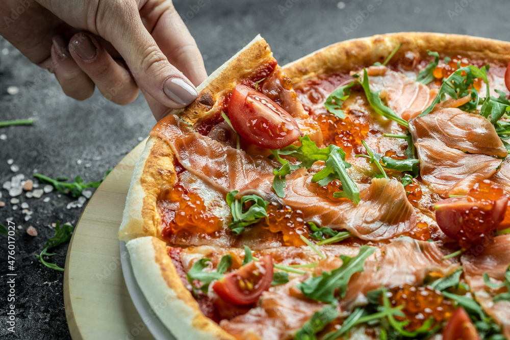 Female hands holding delicious pizza with salmon, red caviar, tomatoes and aragula. italian pizza