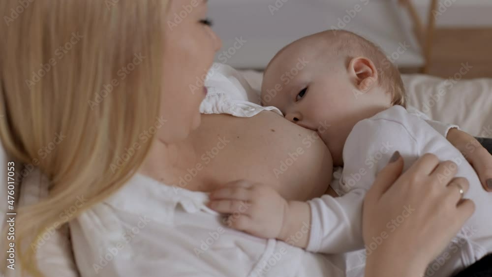 Young blonde woman feeding with breast and stroking her baby boy. Concept of breastfeeding, maternity and child healthcare. Time for togetherness, love and rest for mother and little son Young blonde woman feeding with breast and stroking her baby boy. Concept of breastfeeding, maternity and child healthcare. Time for togetherness, love and rest for mother and little son