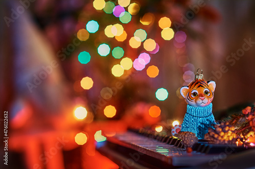 2022. Year of the tiger. Happy Chinese New Year. Christmas tree toy on the piano keys. Colored lights of an electric garland and a silhouette of a gnome in blur. Musical instrument. Selective focus. © Алексей Игнатов