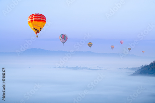 Beautiful hot air balloons flying above foggy landscape in morning ,green mountain in nature with blue sky background.
