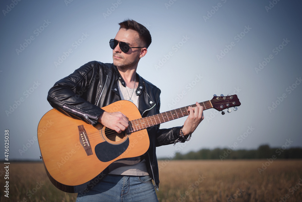 Musician is playing on the guitar among the wheat field.