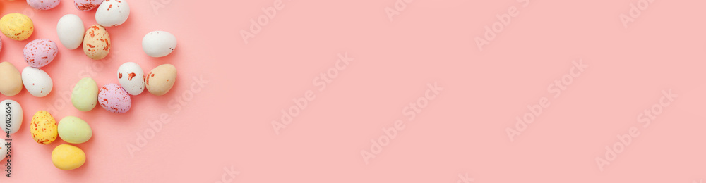 Happy Easter concept. Preparation for holiday. Easter candy chocolate eggs and jellybean sweets isolated on trendy pastel pink background. Simple minimalism flat lay top view copy space banner