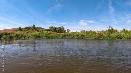Nida river flowing in the nearby of Krzyzanowice Dolne in Poland. The banks of the river are overgrown with lush green grass. Clear, blue sky. Outdoor activity photo