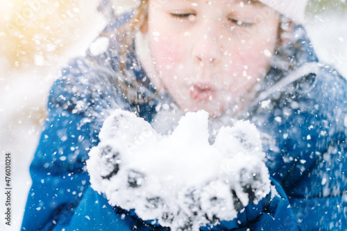 Girl playing on snow in winter time. Happy children in beautiful snowy winter forest on Christmas day. girl blows snow on snowflakes bokeh background. Happy childhood, active winter holidays concept 