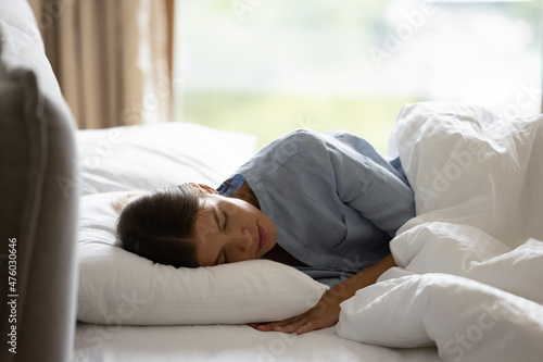 Serene young woman in pajama sleeping in cozy bedroom, lying on comfortable bed with white bedclothes resting with closed eyes, getting recovery, bedtime recreation. Good morning concept