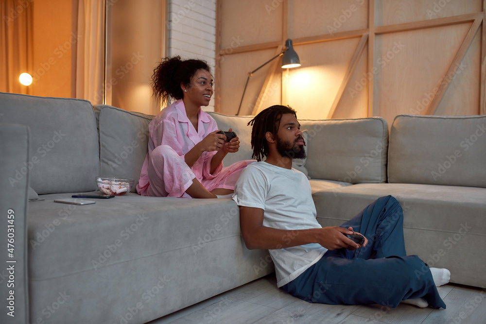 Black couple play video game on joysticks at home