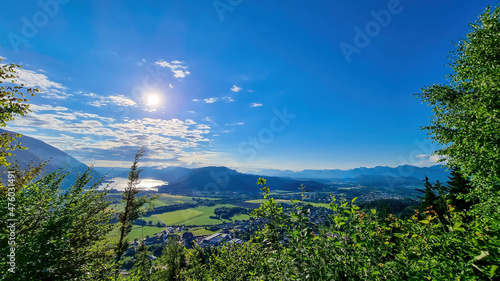 A view on the Lake Ossiach embedded in high Alpine peaks in Carinthia, Austria. The surface if the lake reflects golden sunbeams. Few tree brunches entering the frame. Oswaldiberg photo