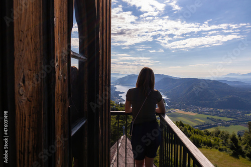 A woman standing at the viewing platform of a chapel at the top of Oswaldiberg with the view on the Lake Ossiach in Austrian Alps, Carinthia. The woman enjoys panoramic view. Morning vibe, Freedom photo