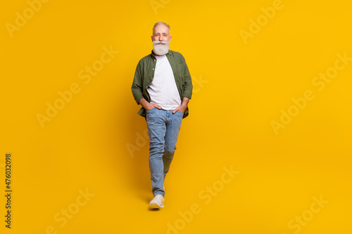 Full length body size photo of senior man smiling going forward isolated vibrant yellow color background